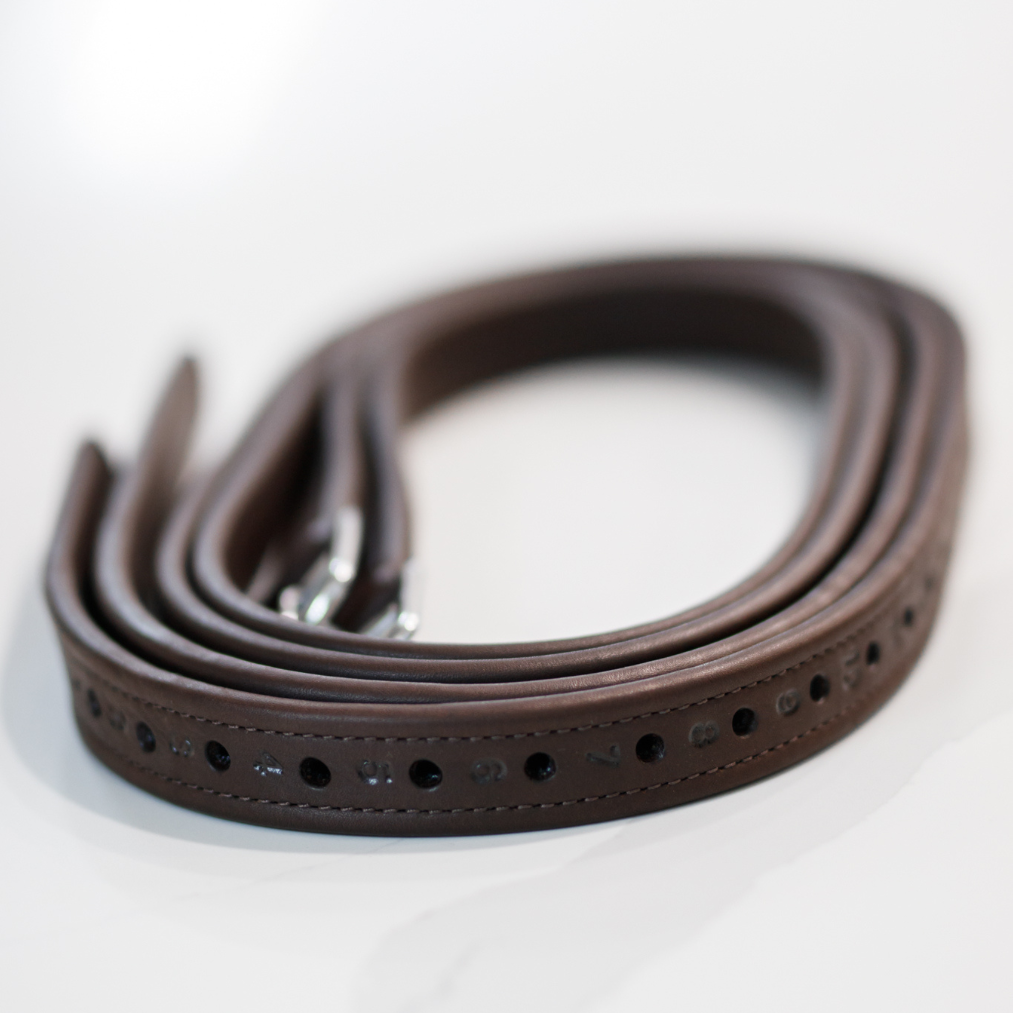 Brown Amerigo stirrup leathers rolled up with numbered holes facing outwards, against a white background
