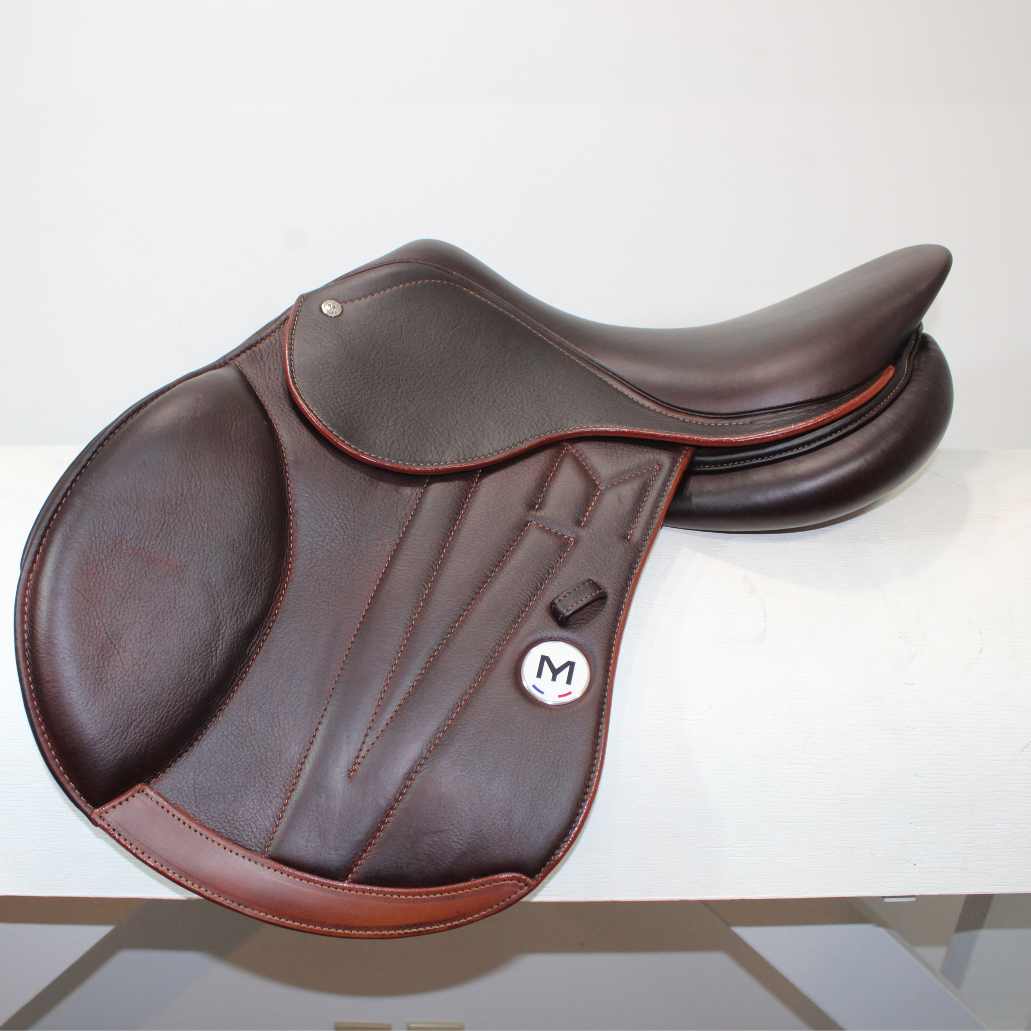 Left side profile view of a Meyer Act 1 jump saddle in brown calf leather, with a white Meyer logo, decorative stitching on flap, and lower flap reinforcement.