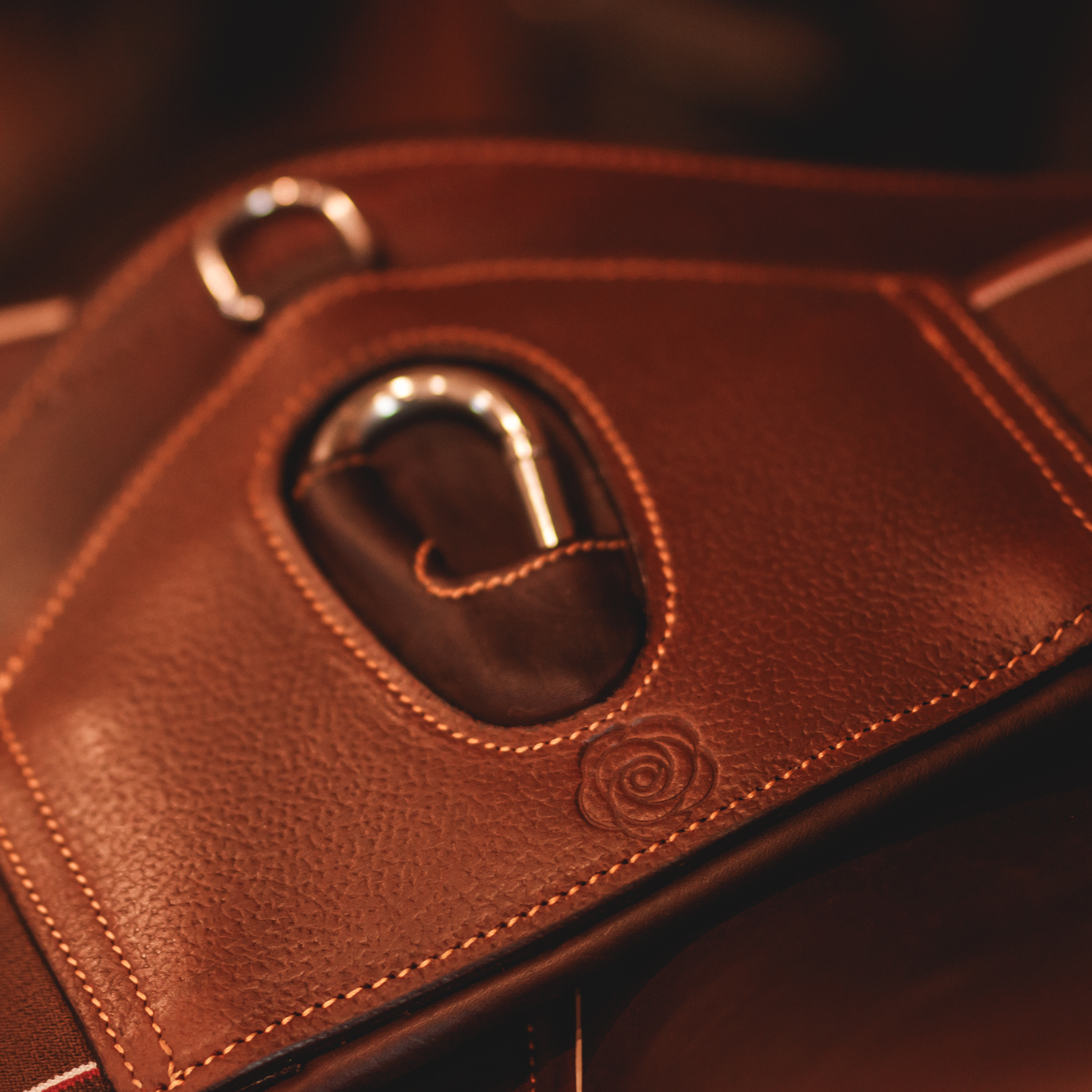 Close-up of the center portion of a brown leather short girth with a metal carabiner, grain leather overlay, and caramel stitching.