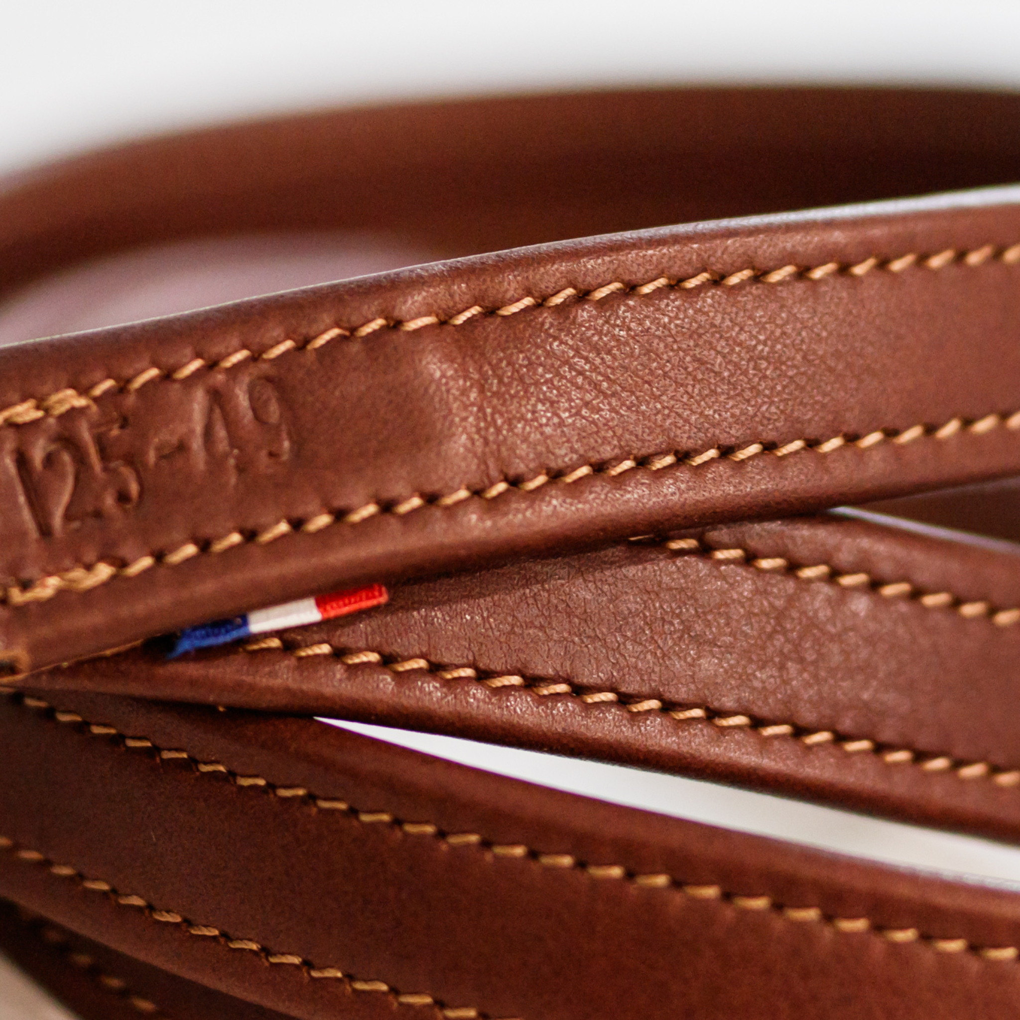 A rolled-up brown Meyer stirrup leather, featuring numbered holes and complimentary stitching.