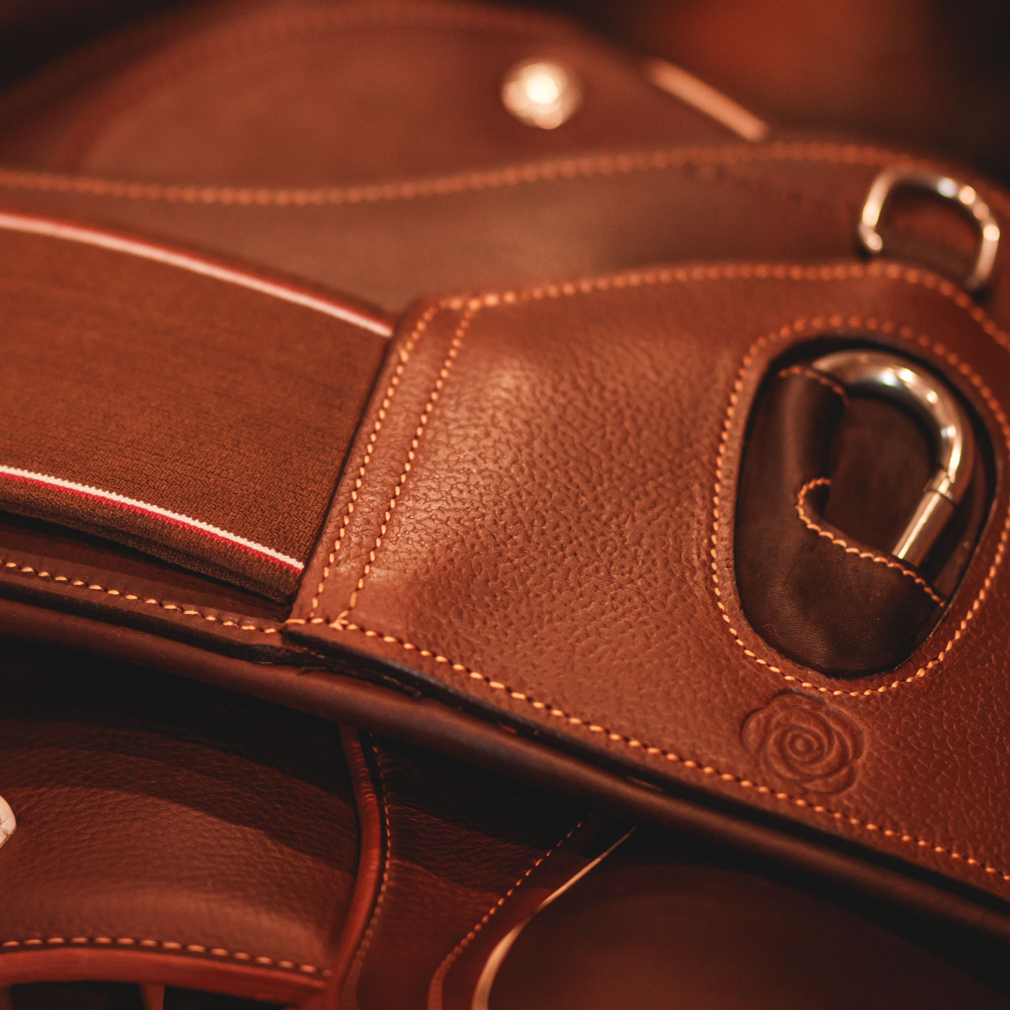 Close-up of the center portion of a brown leather short girth with a metal carabiner, grain leather overlay, and caramel stitching.