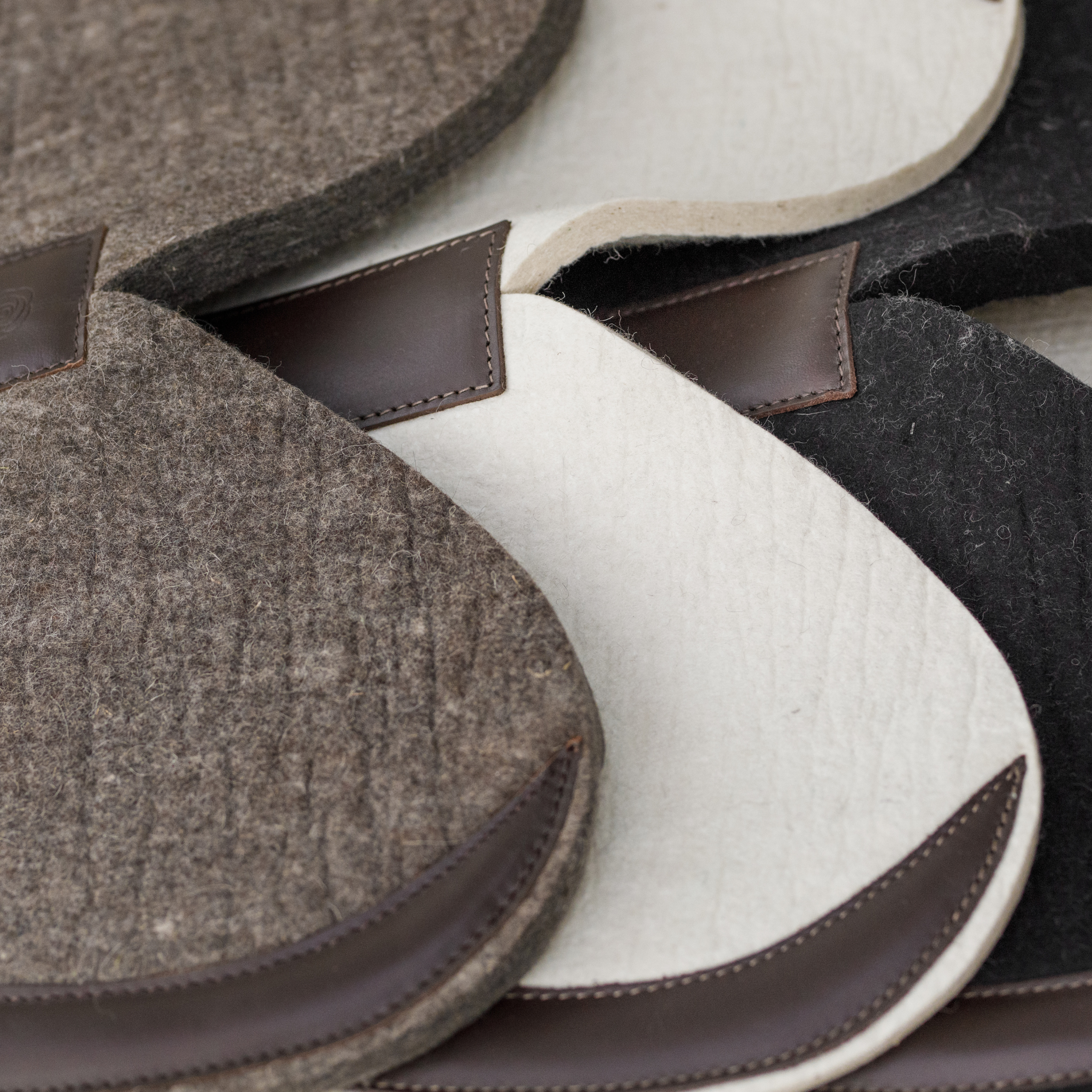 Close-up of 3 felt half pads (natural, cream, and black), each with a wither free design and brown leather trim.