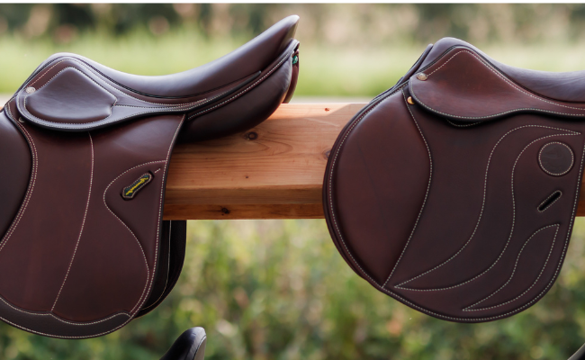 Two brown leather jump saddles on a wooden stand with a blurred natural background