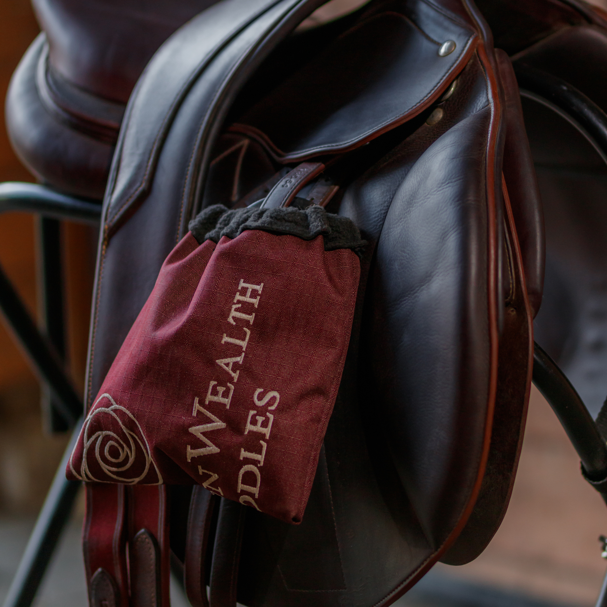 A stirrup cover with the text 'CommonWealth Saddles' and a peony emblem, covering the stirrup on a Meyer saddle.