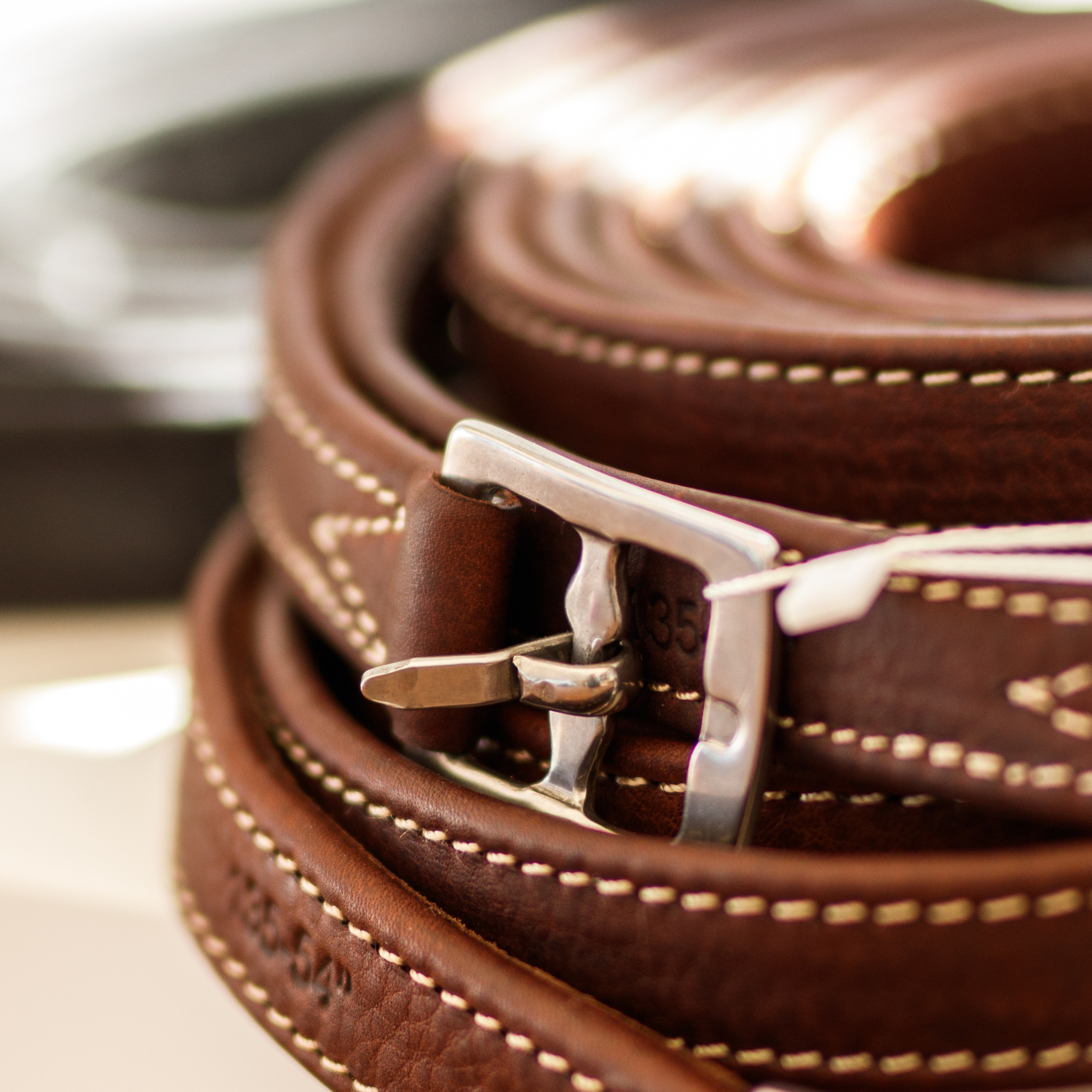 A close up photo of a pair of brown stirrup leathers with white contrast stitching and chrome buckle