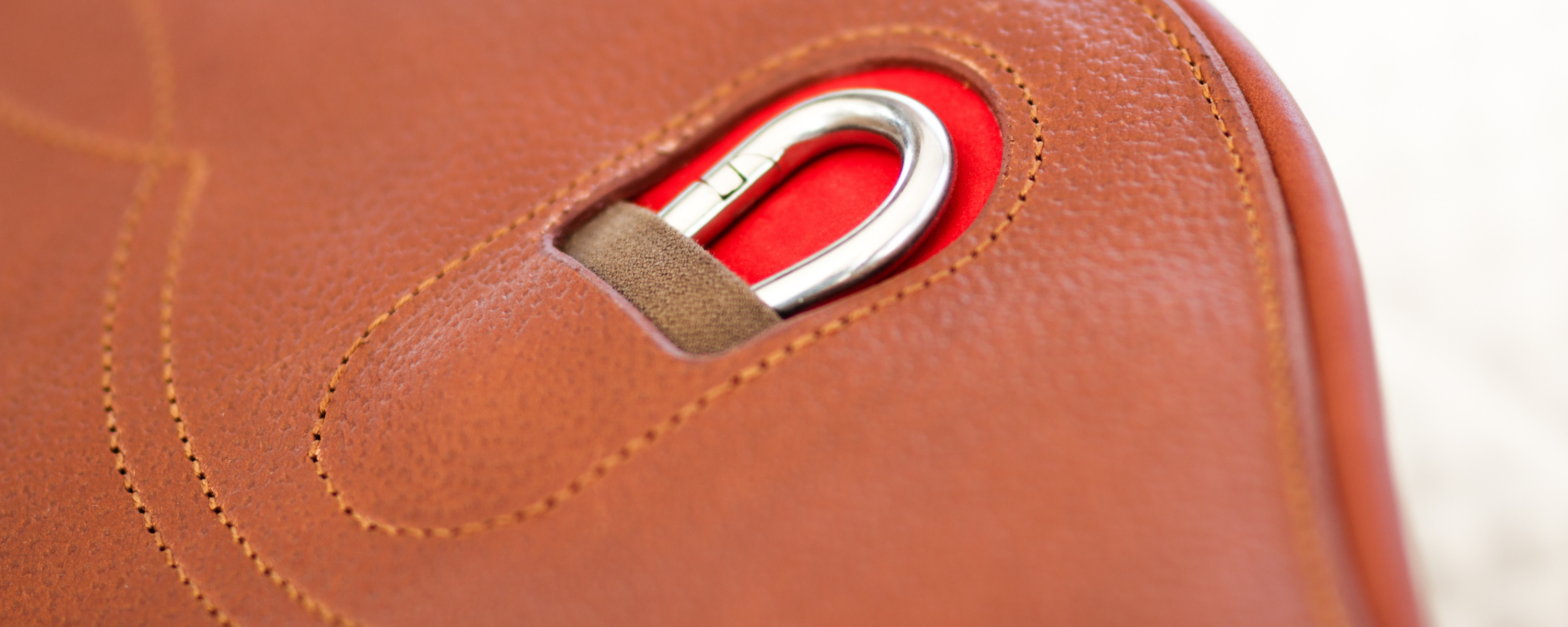 Close-up of a brown fancy stitched leather girth with a chrome carabiner on a red backing.