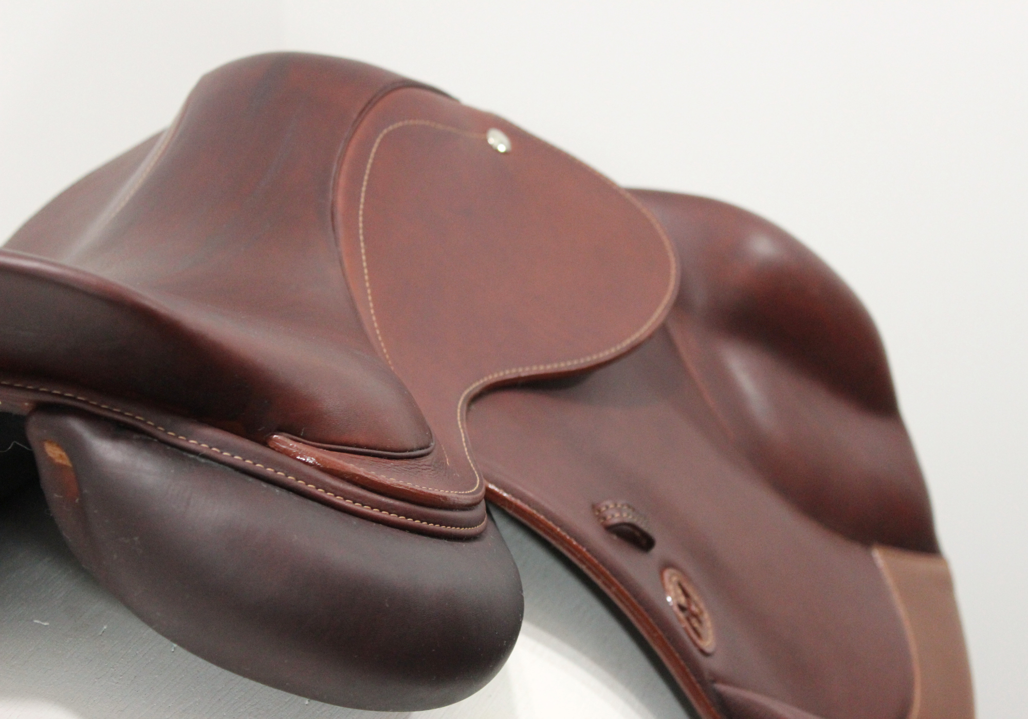 Right angled rear view of a brown leather saddle on a white stand with a light gray background