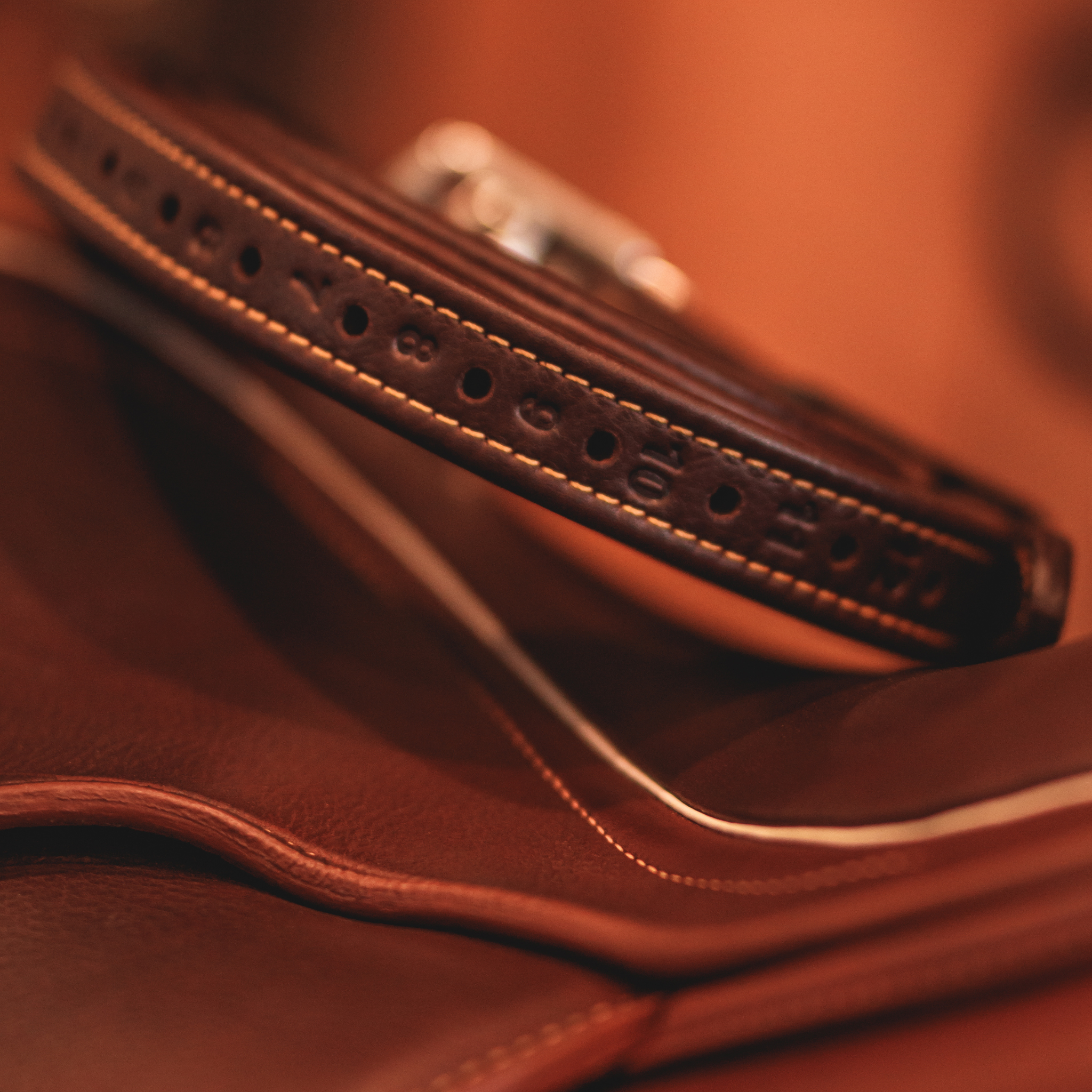 Brown Yoho rolled stirrup leathers sitting on top of a brown saddle against a blurred brown background.