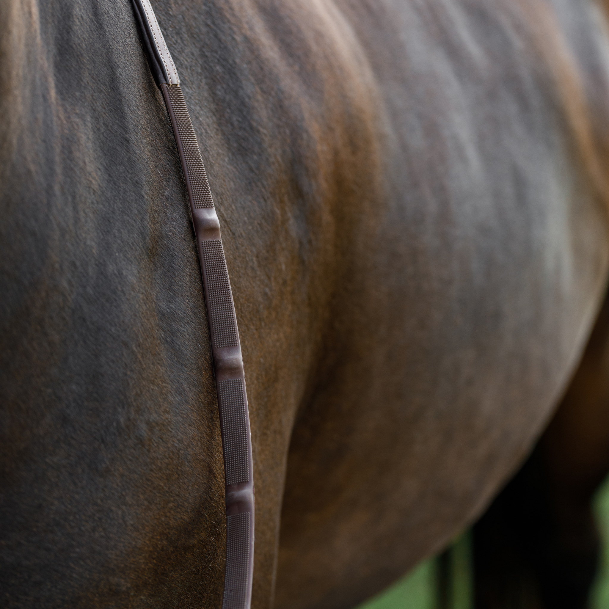 Close up photo to show texture of soft feel rubber reins. Reins are draped over a bay horse's neck.