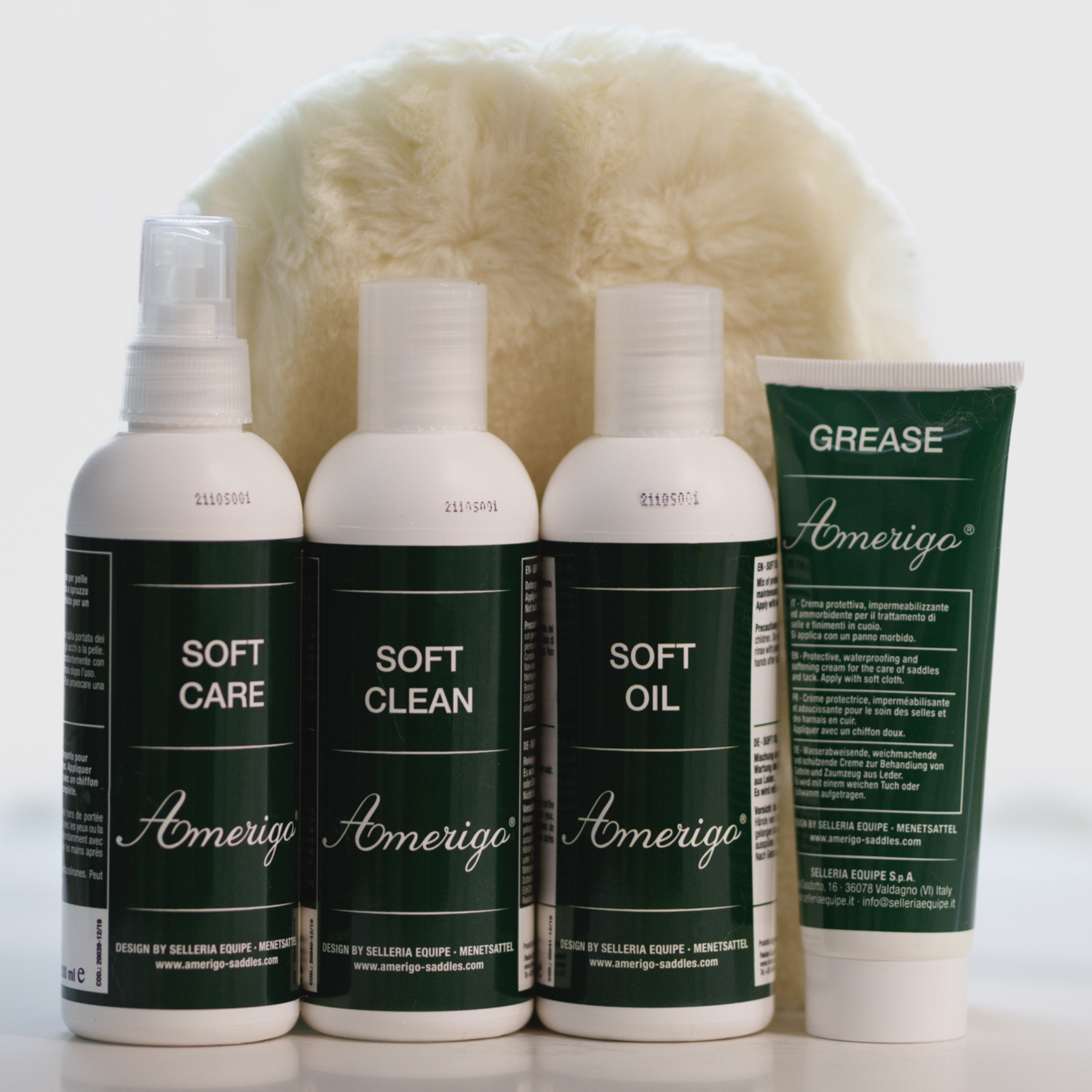 A set of Amerigo leather care products including bottles of cleaner, conditioner, and grease, along with a tube labeled 'Soft Oil' and a sheepskin mitt.