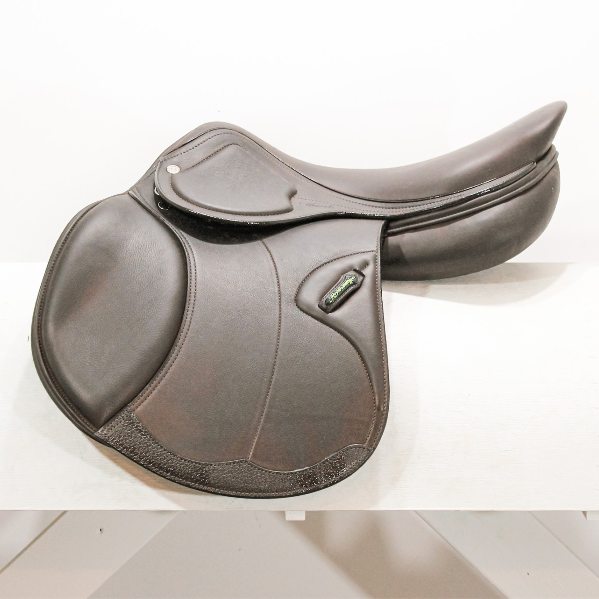 Left side profile view of an Amerigo HC dual flap jump saddle in dark brown calf leather, with a green and yellow Amerigo logo loop and lower flap reinforcement