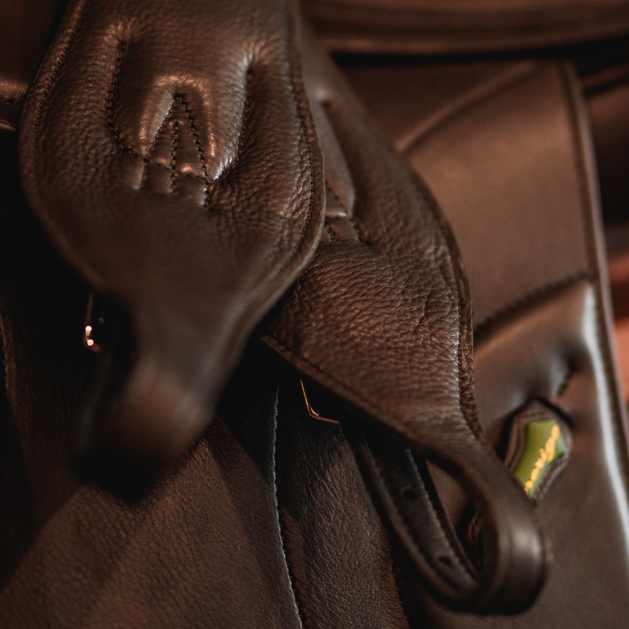 Close-up of black Cavell stability leathers draped over a black Amerigo dressage saddle, with a focus on the supple texture of the stirrup leathers.