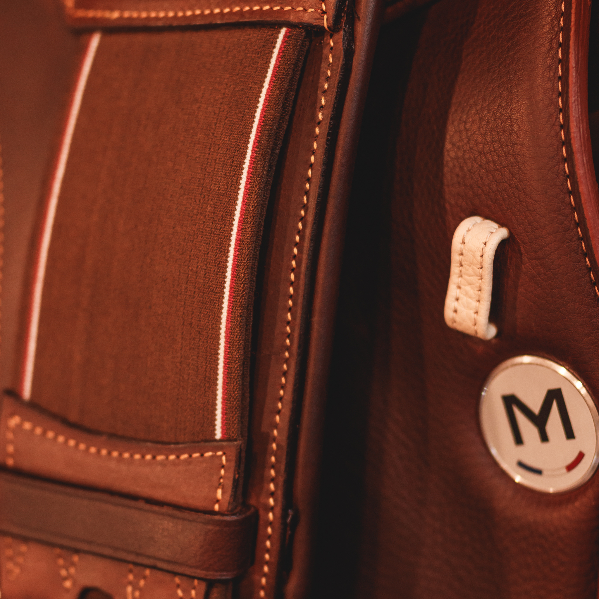 Close-up of the brown girth elastics against a Meyer saddle with a white logo and ivory loop. 