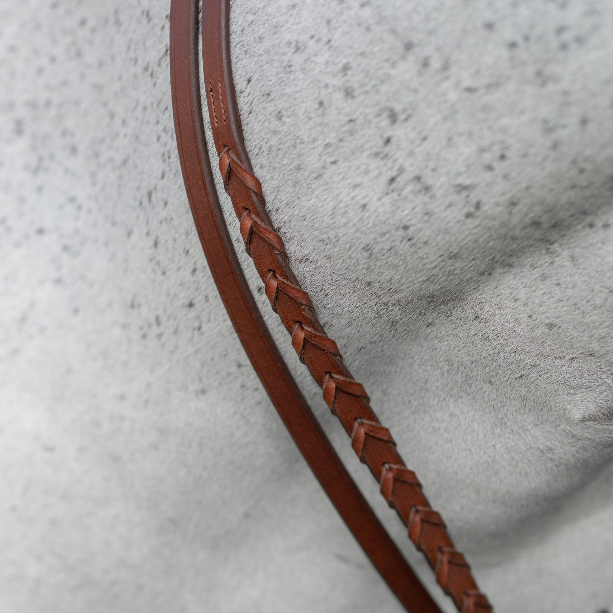Close-up of a pair of brown laced reins and brown curb reins against a grey horse's neck.