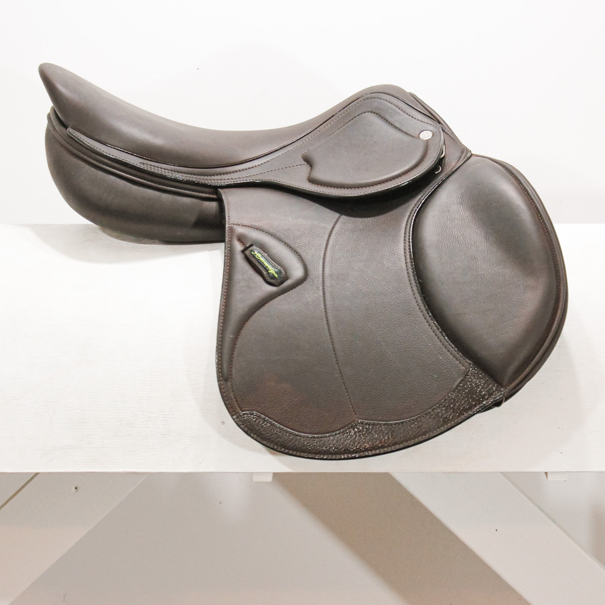 Right side profile view of an Amerigo HC dual flap jump saddle in dark brown calf leather, with a green and yellow Amerigo logo loop and lower flap reinforcement