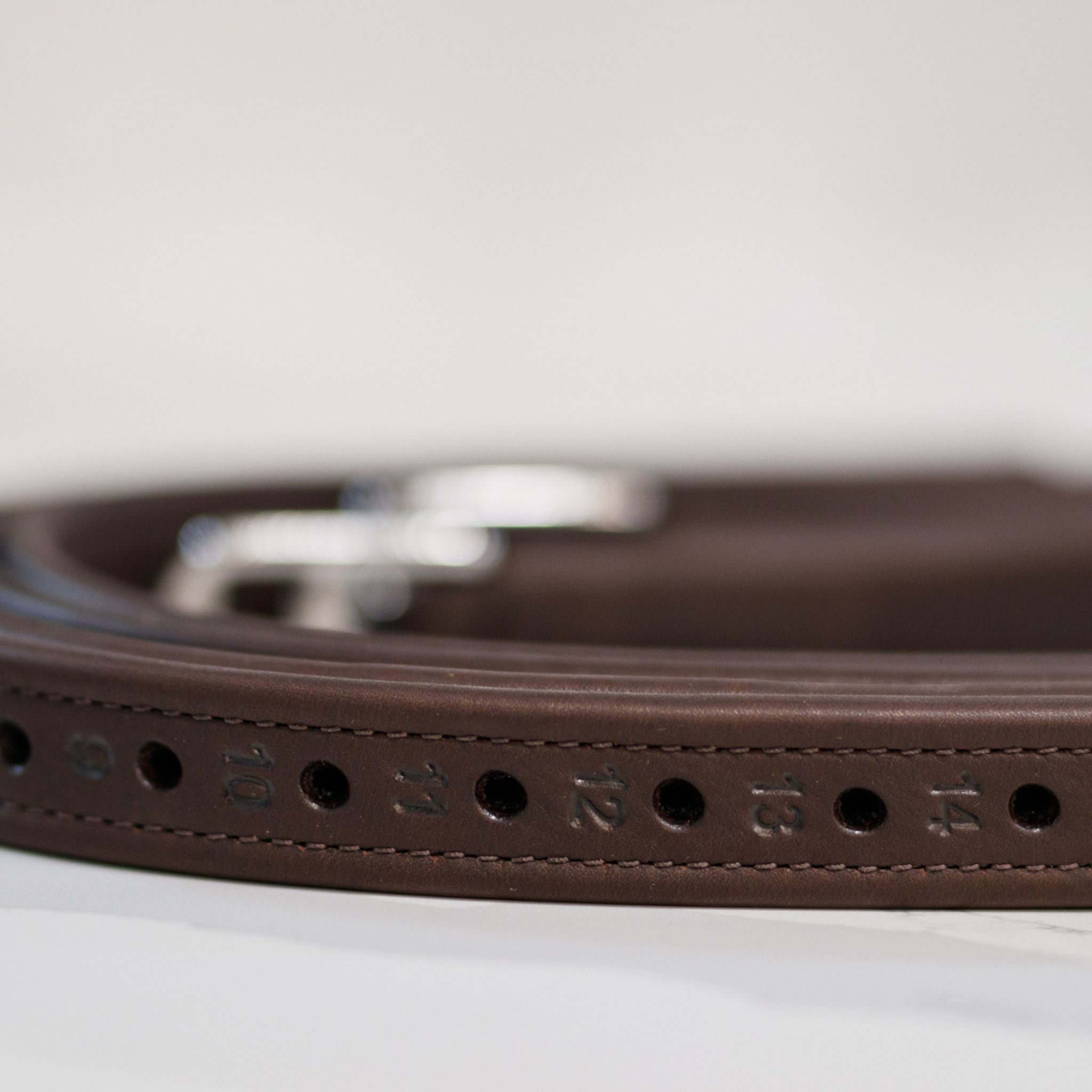 Brown Amerigo stirrup leathers rolled up with numbered holes facing outwards, against a white background. Photo is close up and focused on the numbered holes.