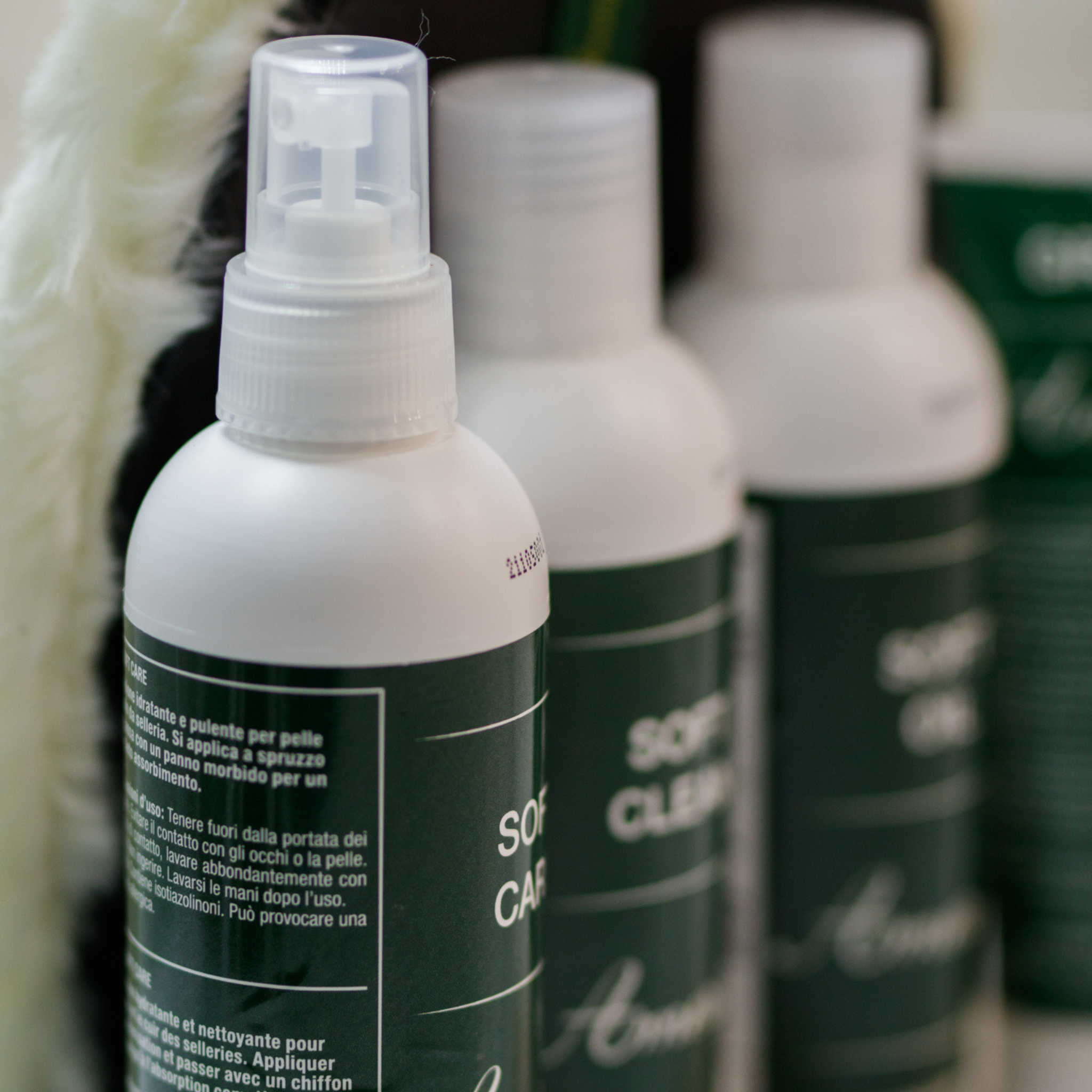 A close up photo of Amerigo leather care products; the photo is focused on a bottle of 'Soft Care', with the other products blurred into the background.