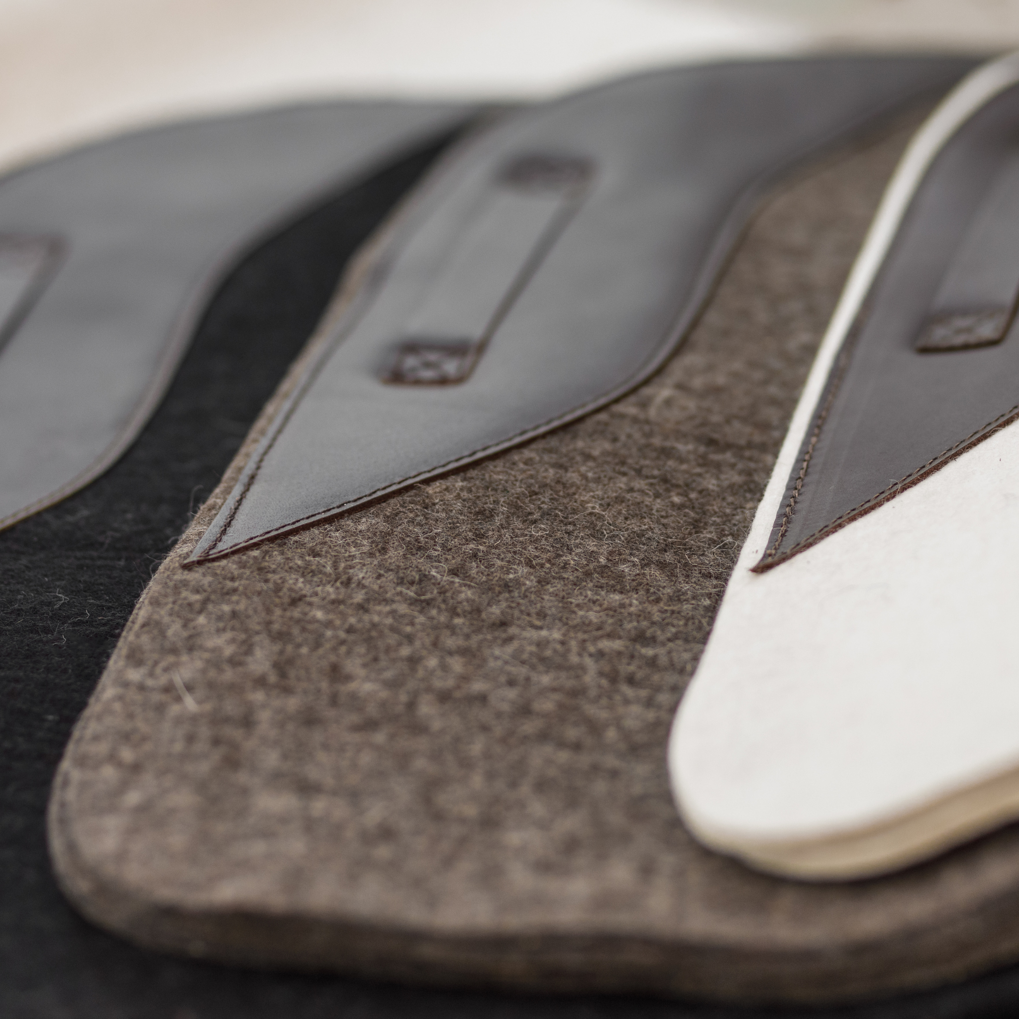 Close-up of 3 felt saddle pads (black, natural, and cream) with leather accents.