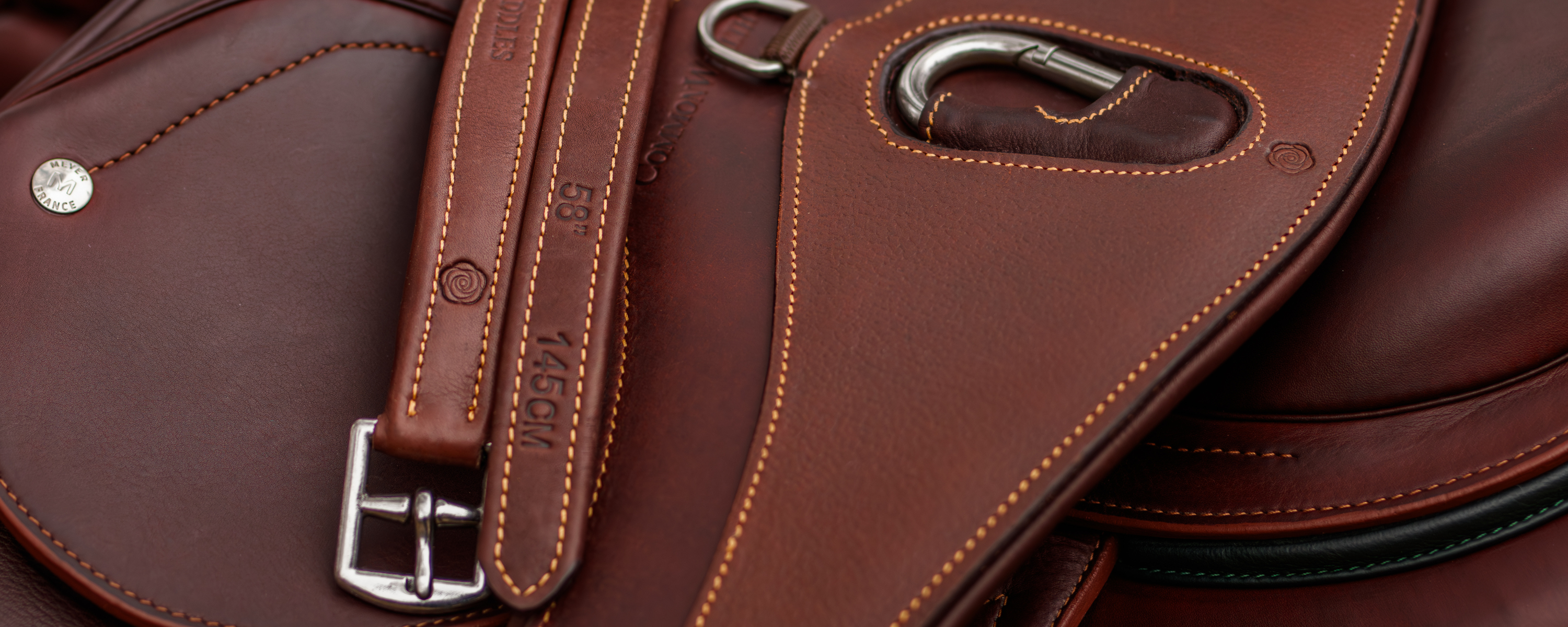 Close-up of a brown Rideau girth and Yoho stirrup leathers draped over a Meyer saddle. 
