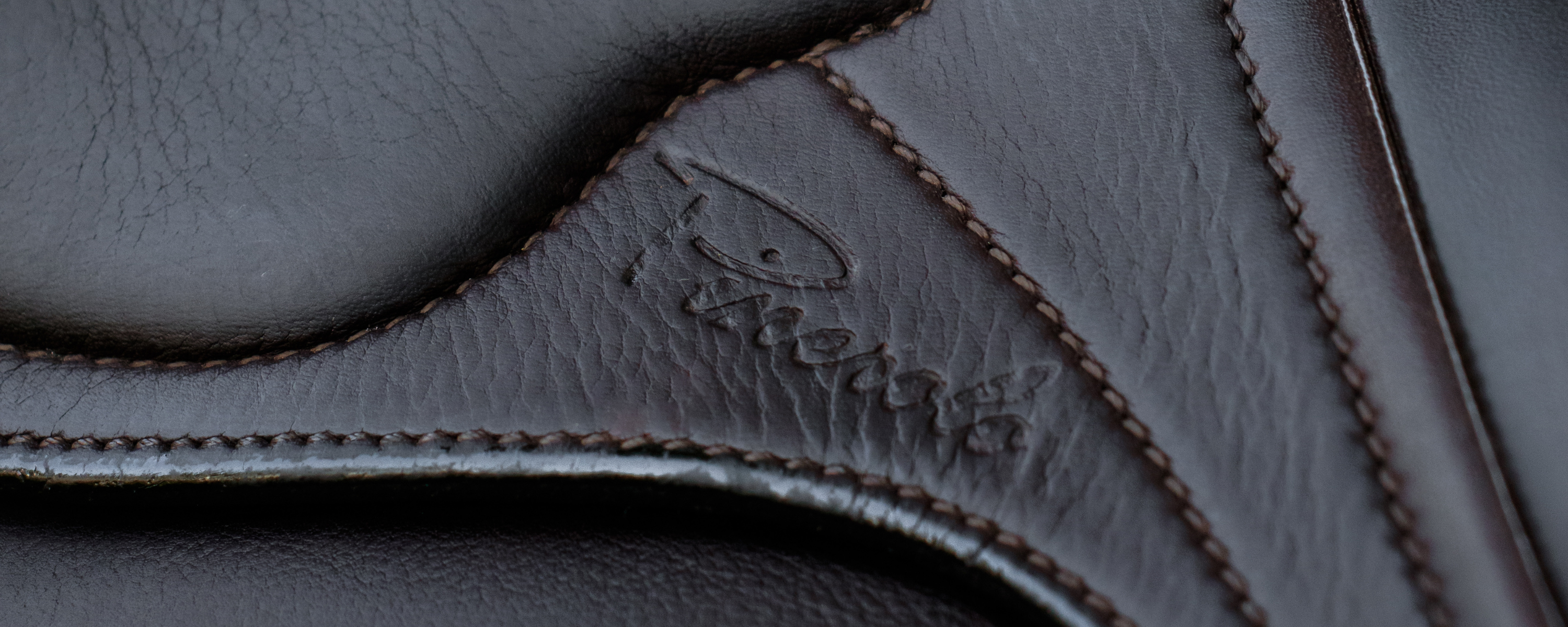 Close-up of dark brown Amerigo leather with stitched paneling and an embossed script logo reading 'Pinerolo'.