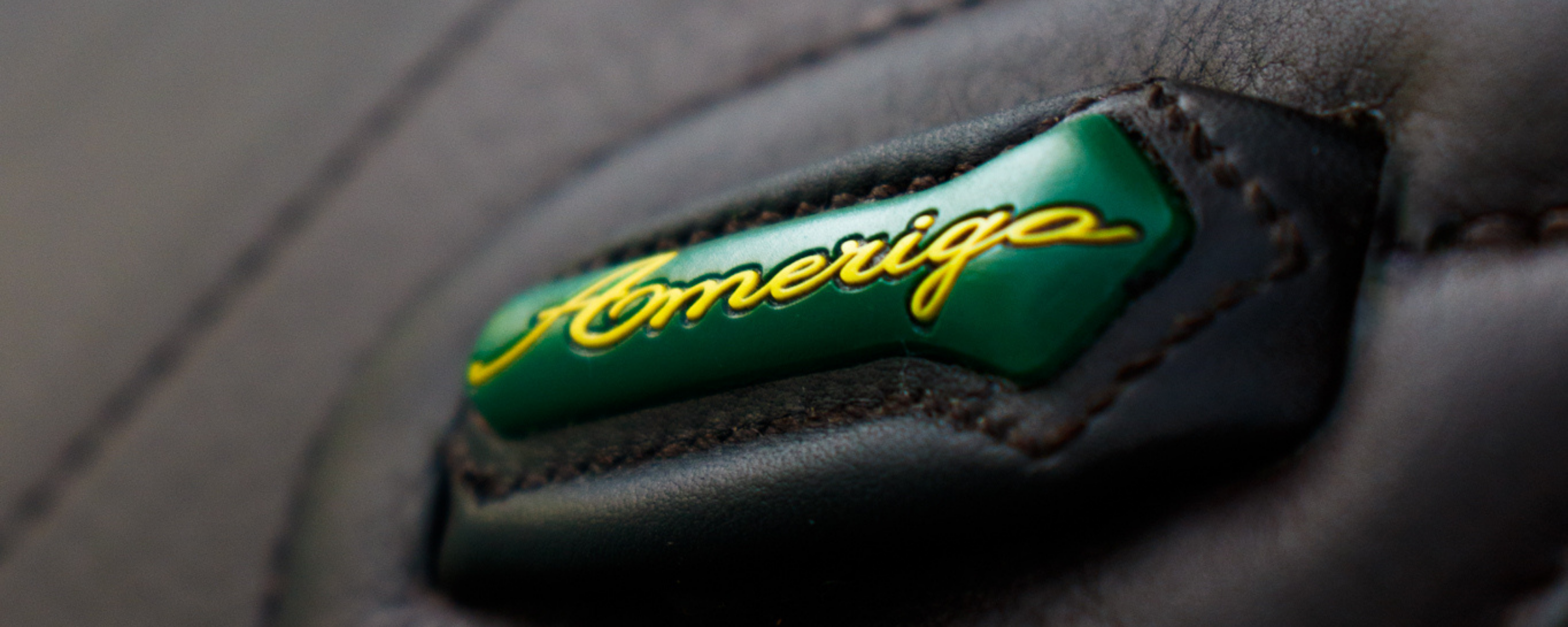 Close-up of a brown stirrup leather keeper, with green patch featuring yellow cursive 'Amerigo' text. 