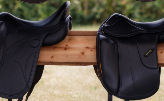 Two black dressage saddles on a wooden stand with a blurred natural background