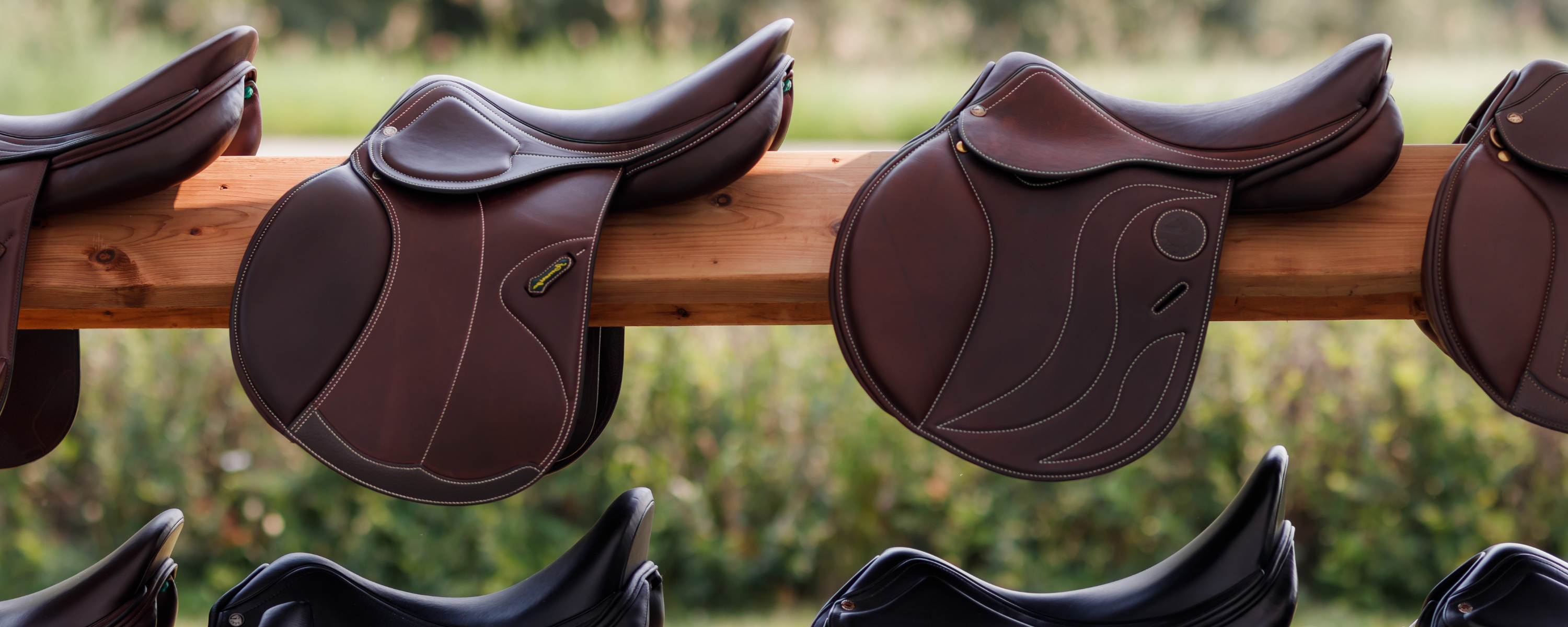 Brown jump saddles on a wooden stand with a blurred natural background