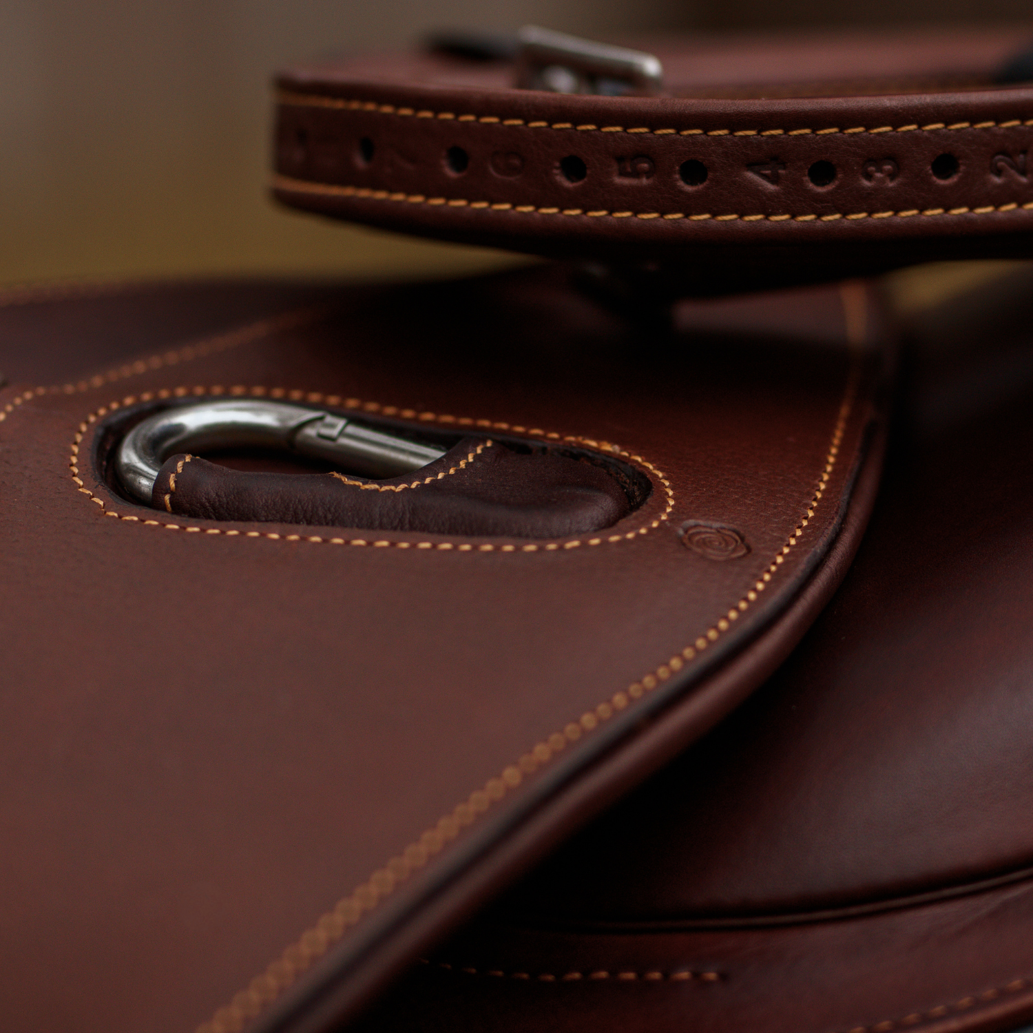Close-up of a brown leather girth and brown stirrup leathers stacked on top of a saddle. 