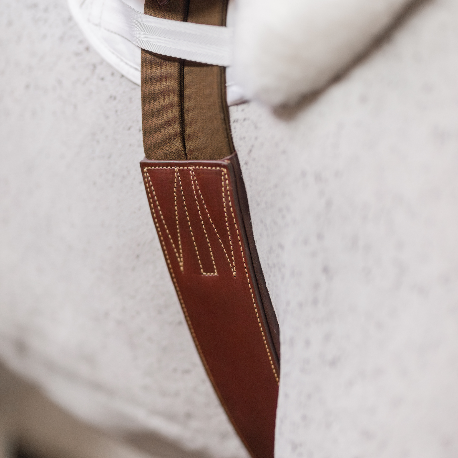 Close-up of a brown leather girth with caramel contrast stitching on a grey horse.