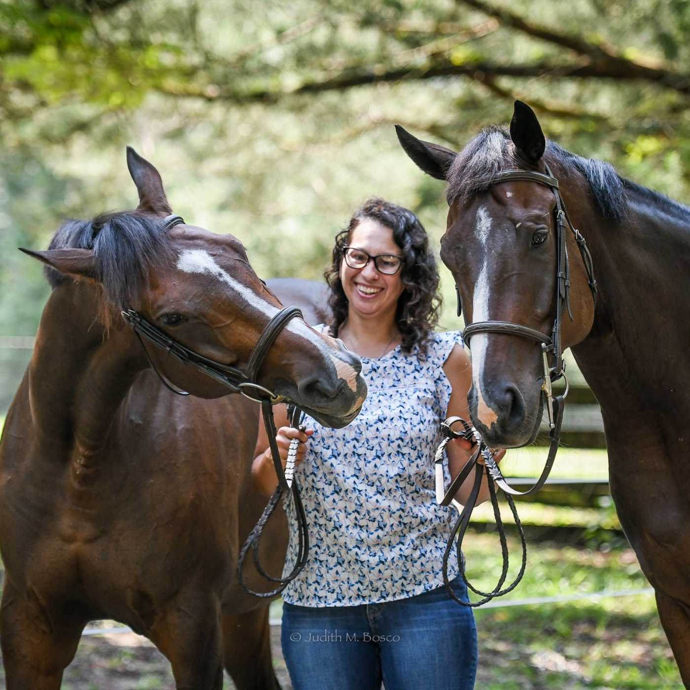 Woman standing between two horses in a natural setting.
