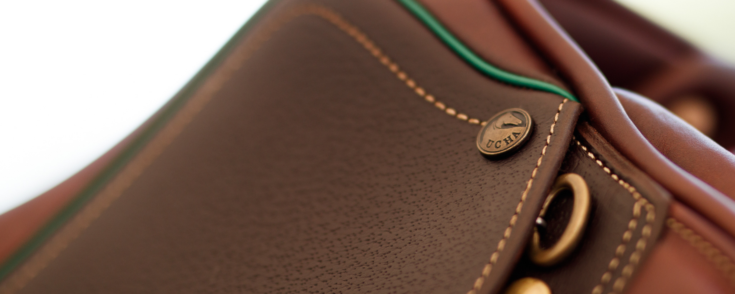 Close up of a brown Ucha Pampa jump saddle with green piping along the seat and grain leather flaps.