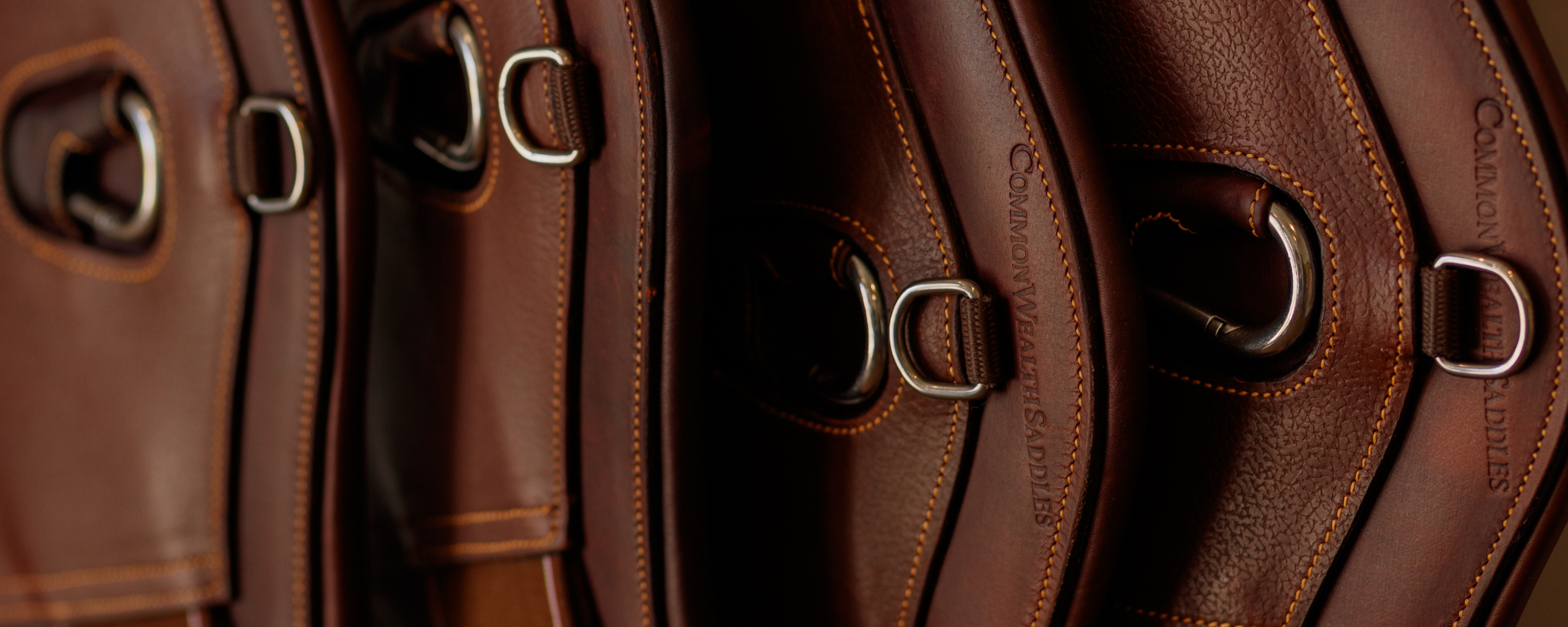 Close-up of multiple brown leather CommonWealth girths with visible stitching and hardware.