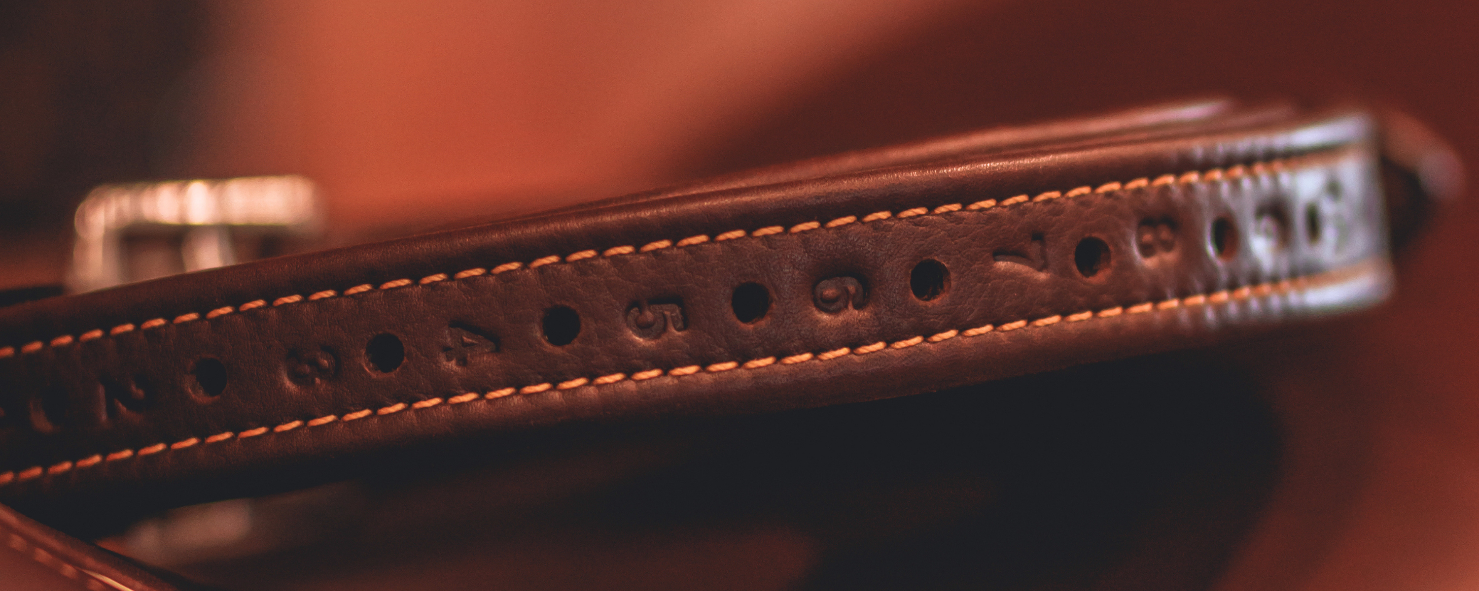 Close-up of a brown Yoho stirrup leather with caramel contrast stitching against a brown blurred background.