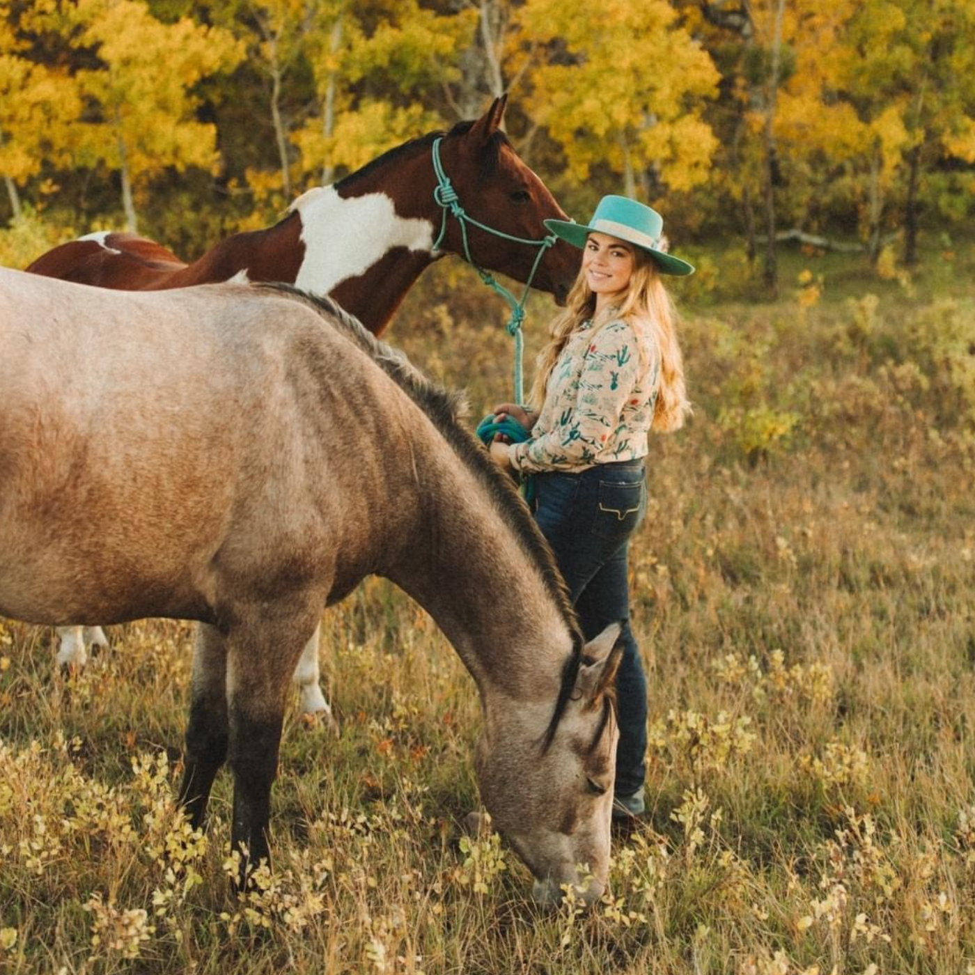 Woman standing with two horses in a field with trees in the background