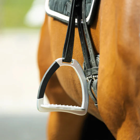 A silver Ophena safety stirrup with a removable, black rubber outer branch, dangling from the saddle to the side of a chestnut horse 