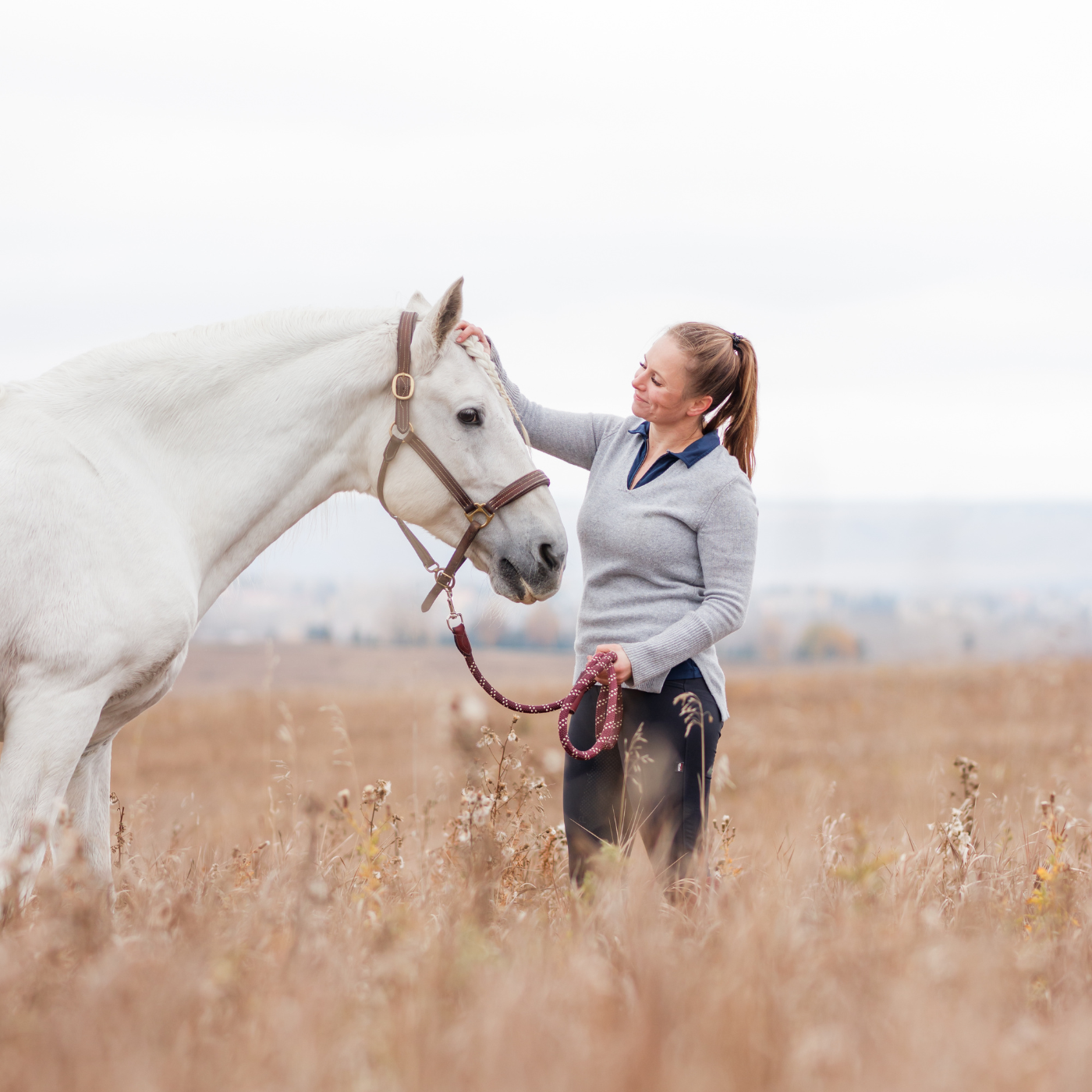 Woman standing with a white horse in a field