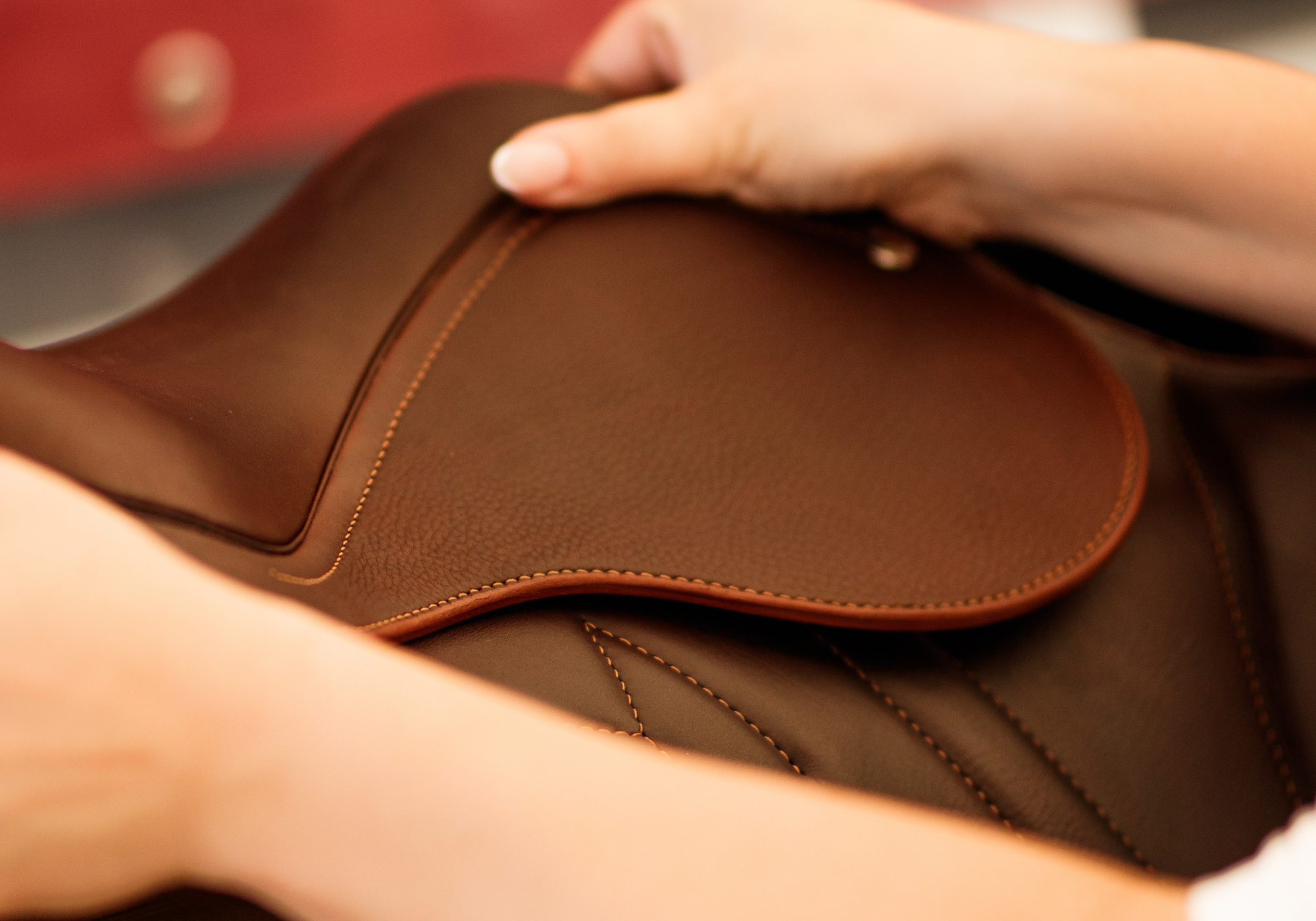 Close up of a brown leather saddle being picked up against a blurred background