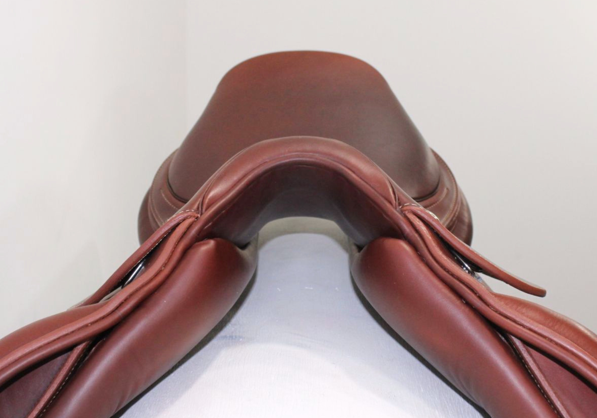 Front view of a brown leather saddle on a white stand with a light gray background