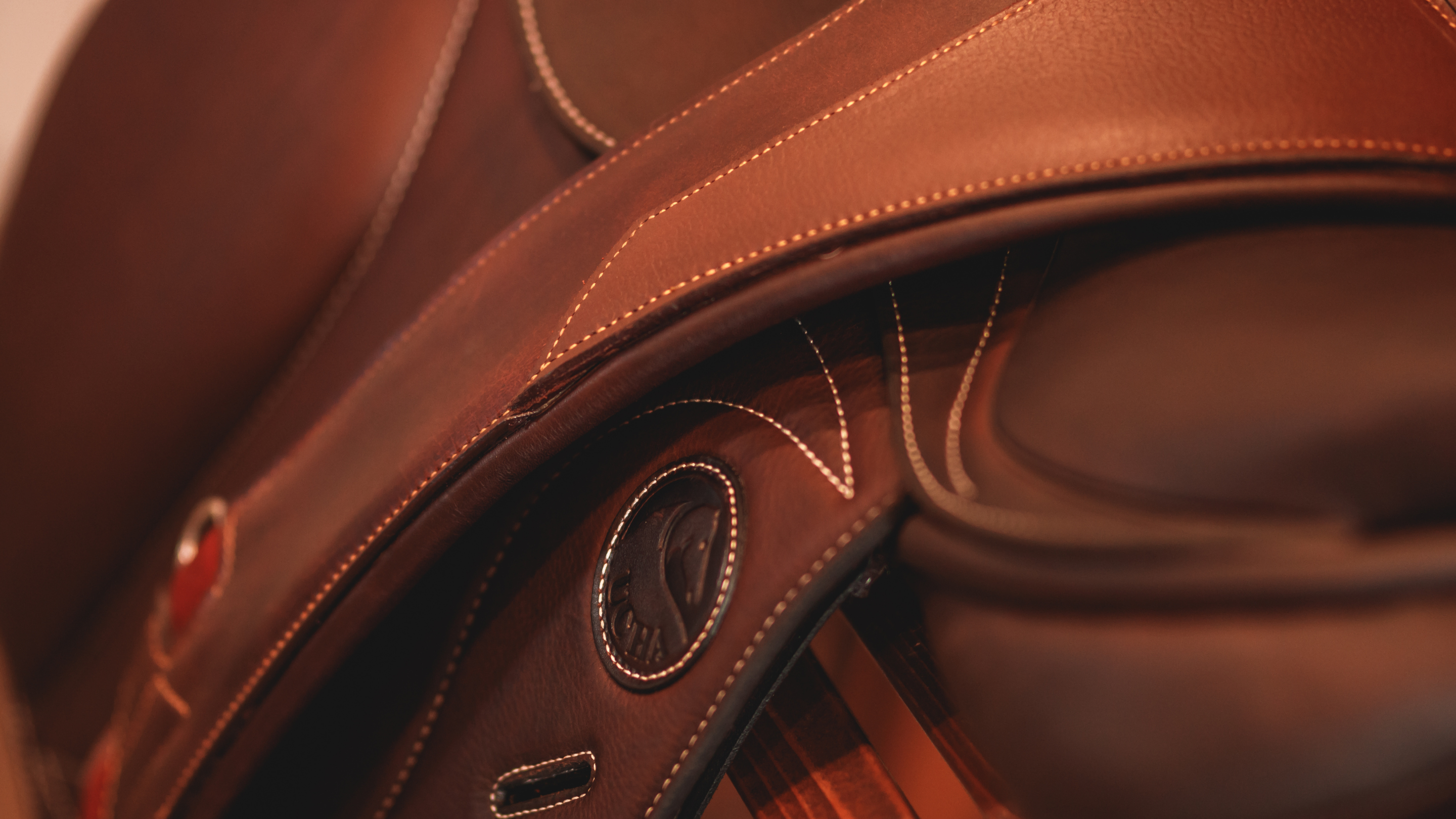 Close up photo of a rich brown Ucha saddle with a CommonWealth Rideau girth draped over top.