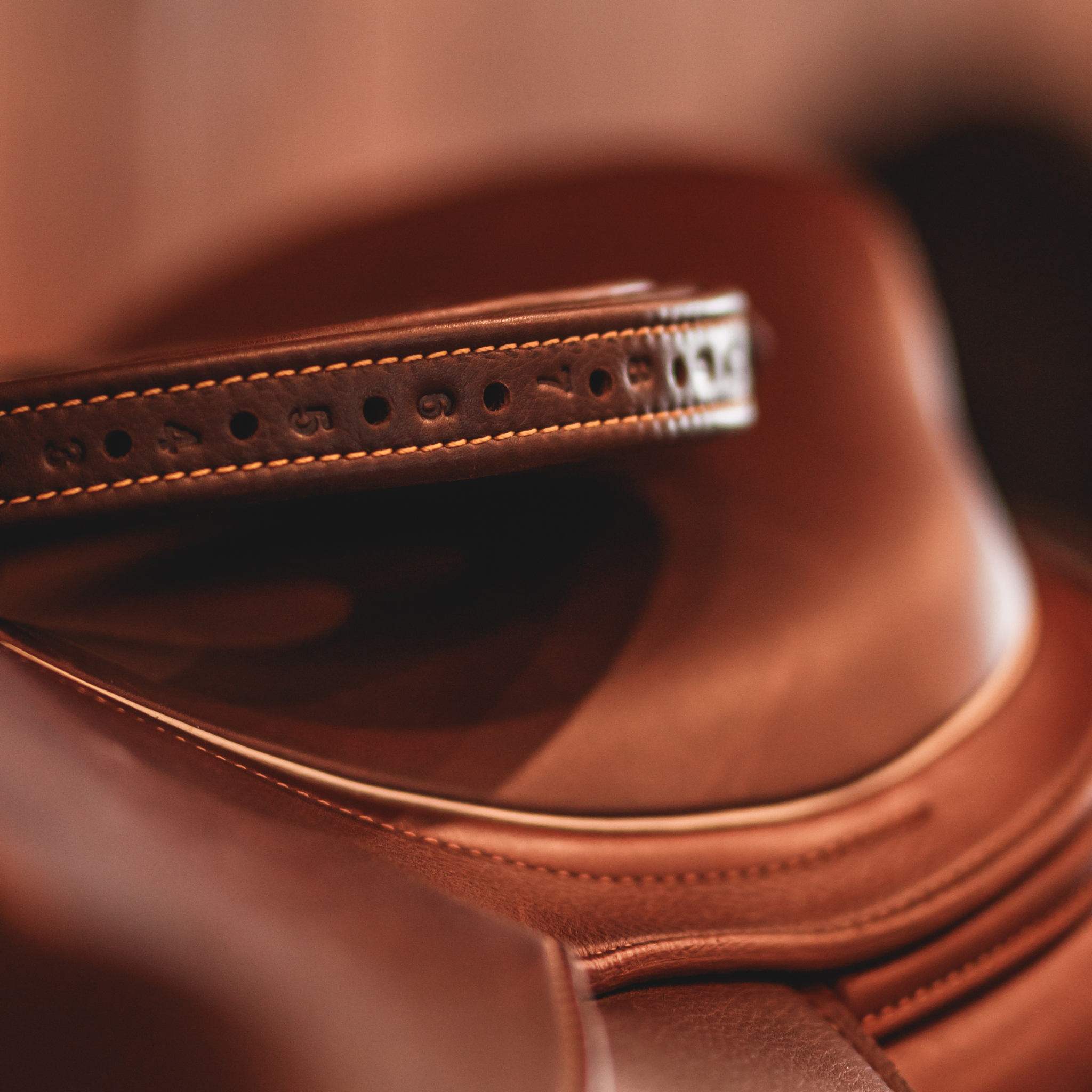Brown Yoho rolled stirrup leathers sitting on top of a brown saddle against a blurred brown background. 